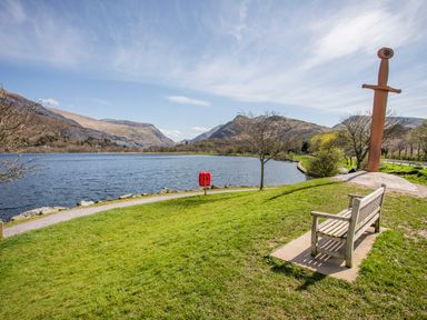 A bench and a sword sculpture near a lake with mountains in the background at 5 Thomas Street in Llanberis
