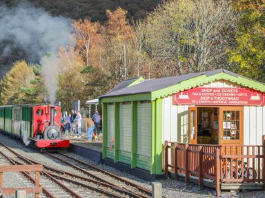 A small railway station with a red steam train and a green and cream shop building at 5 Thomas Street in Llanberis