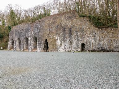 A large stone wall with multiple arched openings and small gravel ground in front of it with trees in the background at Seacroft Stepaside near Kilgetty