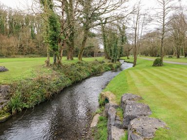 A small river flowing between grassy banks with trees and rocks at Seacroft in Stepaside near Kilgetty