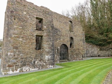 An old stone wall with arched windows and a gated entrance next to a striped green lawn and trees at Seacroft in Stepaside near Kilgetty