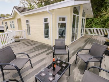 An outdoor deck with four chairs and a table with a bottle and four glasses at Seacroft in Stepaside near Kilgetty