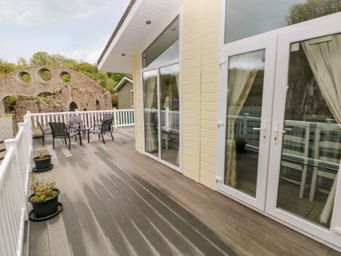 A wooden deck with potted plants and a table with four chairs outside a building with large glass doors at Seacroft in Stepaside near Kilgetty