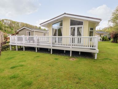 A small house with large windows and a white railing on a raised deck on a grassy lawn at Seacroft in Stepaside near Kilgetty