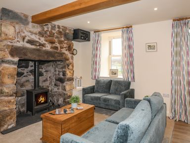 A living room with a stone fireplace and wood burning stove two sofas a wooden coffee table and patterned curtains at Pennant Igyn in Mynytho near Abersoch