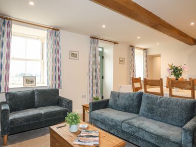 A living room with two sofas a wooden coffee table with plants and magazines a dining table with chairs and flowers on it at Pennant Igyn in Mynytho near Abersoch