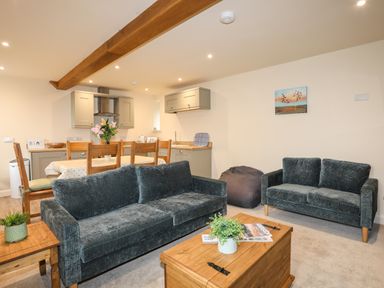 A living room with two sofas a wooden coffee table plants and a dining table with chairs and flowers at Pennant Igyn in Mynytho near Abersoch