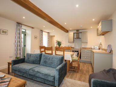A living room and kitchen with a blue sofa wooden dining table and grey cabinets at Pennant Igyn in Mynytho near Abersoch