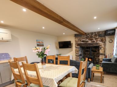 A dining area with a table and chairs and a living space with sofas and a stone fireplace at Pennant Igyn in Mynytho near Abersoch