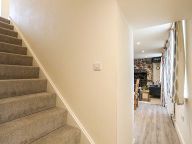 A carpeted staircase next to a hallway with wooden floor leading to a room with a stone fireplace and furniture at Pennant Igyn in Mynytho near Abersoch