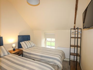 A bedroom with two single beds striped bedding and a nightstand lamp at Pennant Igyn in Mynytho near Abersoch