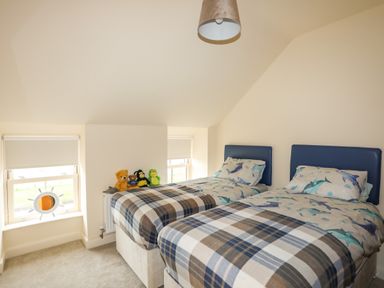 A bedroom with two single beds covered in plaid blankets and shark-themed bedding with stuffed animals on a windowsill at Pennant Igyn in Mynytho near Abersoch