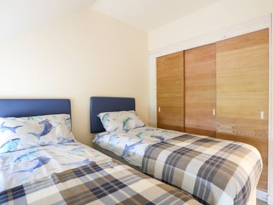 A bedroom with two single beds with blue headboards and shark print bedding and a wooden sliding door wardrobe at Pennant Igyn in Mynytho near Abersoch
