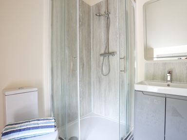 A bathroom with a glass shower enclosure a toilet with a striped towel and a sink with a mirror at Pennant Igyn in Mynytho near Abersoch