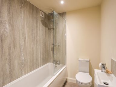 A bathroom with a bathtub and shower combination next to a toilet and small sink at Pennant Igyn in Mynytho near Abersoch