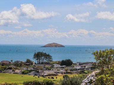 A coastal village with houses trees and cows in a field overlooking sailboats on the sea and an island in the distance at Pennant Igyn in Mynytho near Abersoch