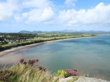 A coastal landscape with a sandy beach water and a village with houses at Pennant Igyn Mynytho near Abersoch