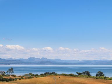 A coastal landscape with grassy fields trees and a house by the shore at Pennant Igyn in Mynytho near Abersoch