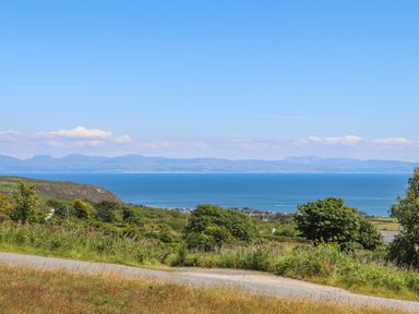 A coastal landscape with a road in the foreground trees and a view of the sea and distant mountains at Pennant Igyn in Mynytho near Abersoch
