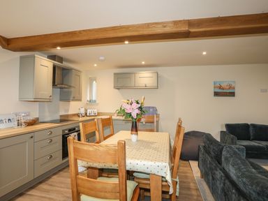 A kitchen with grey cabinets and a wooden dining table with chairs and flowers in a vase at Pennant Igyn in Mynytho near Abersoch