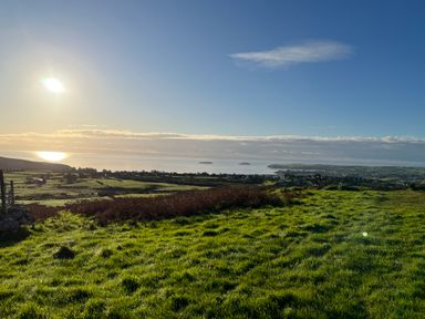A landscape view of green fields with the sun shining over the sea and islands in the distance at Pennant Igyn in Mynytho near Abersoch