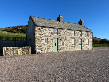 A stone cottage with green doors and windows in a rural area at Pennant Igyn in Mynytho near Abersoch
