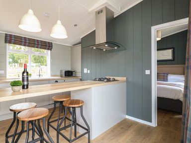 A kitchen area with a wooden breakfast bar and stools next to a stove and a door leading to a bedroom at Holly Lodge in Winthorpe near Newark-On-Trent
