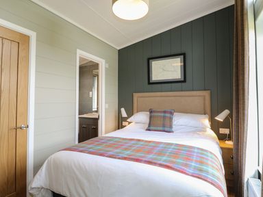 A bedroom with a double bed plaid throw pillow and blanket bedside tables with lamps and an open door to a bathroom at Holly Lodge in Winthorpe near Newark-On-Trent
