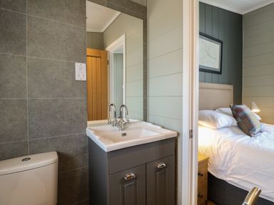 A bathroom with a sink and toilet next to a bedroom with a bed and bedside table at Holly Lodge in Winthorpe near Newark-On-Trent