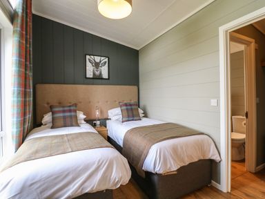 A bedroom with two single beds with plaid pillows and throws a nightstand in between and a bathroom visible through a doorway at Holly Lodge Winthorpe near Newark-On-Trent