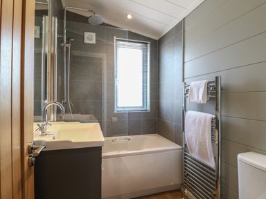 A bathroom with a bathtub shower combination a sink a towel rack with towels and a window at Holly Lodge in Winthorpe near Newark-On-Trent