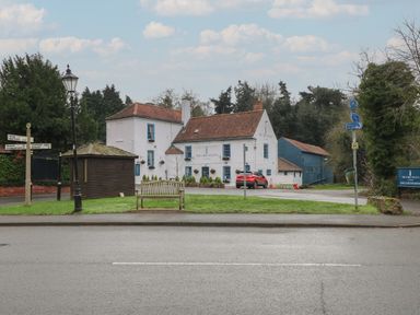 A pub building with a red car parked outside and a wooden bench on a grassy area by the road at Holly Lodge in Winthorpe near Newark-On-Trent