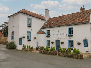The exterior of The Lord Nelson pub with white walls blue window frames hanging flower baskets and small green shrubs at Winthorpe near Newark-On-Trent