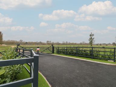 A paved driveway with black metal gates and fencing overlooking green fields at Holly Lodge in Winthorpe near Newark-On-Trent