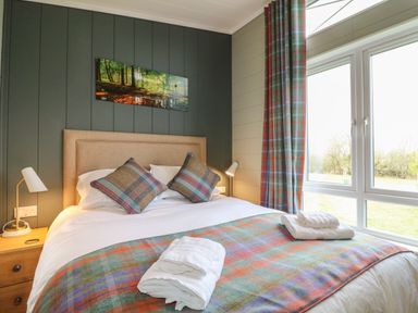 A bedroom with a double bed two plaid cushions folded towels on the bed bedside tables lamps and a large window at Cedar Lodge in Newark-On-Trent