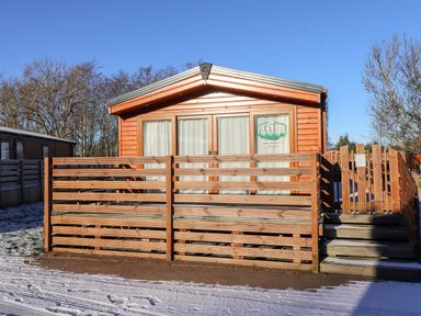 A wooden cabin with a fenced porch and steps in front surrounded by snow at Orion in Felmoor Park