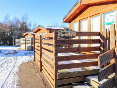 A pathway with three wooden cabins and fenced porches with snow on the ground at Orion Felmoor Park