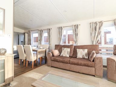A living room with a brown sofa and patterned curtains near a dining table with four chairs at Orion in Felmoor Park