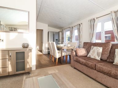 A living room with a sofa and pillows next to a dining table with chairs and a cabinet at Orion in Felmoor Park