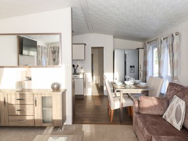 A dining area with a table set for four next to a sofa and a sideboard with a lamp and mirror at Orion in Felmoor Park