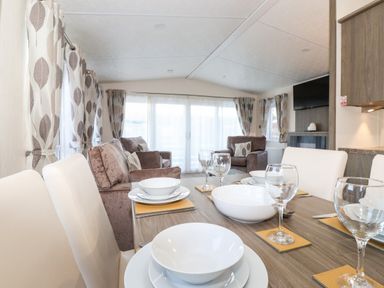 A dining table set with bowls plates and glasses with sofas and curtains in the background at Orion in Felmoor Park