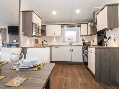 A kitchen with white cabinets a microwave a stove and a dining table with glasses and plates at Orion Felmoor Park
