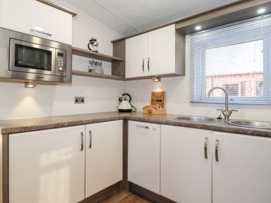 A kitchen with a microwave kettle double sink and window with blinds at Orion in Felmoor Park