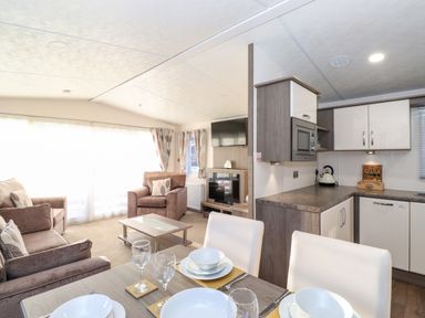 An open plan living room and kitchen with dining table set with dishes and glasses at Orion in Felmoor Park