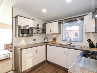 A kitchen with white cabinets a microwave a kettle a window with blinds and a stove at Orion in Felmoor Park