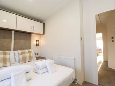 A bedroom with a bed with plaid pillows folded towels on white bedding bedside cabinets and a wall lamp at Orion Felmoor Park