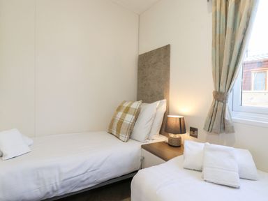 A bedroom with two single beds bedside table lamp window and curtains at Orion in Felmoor Park