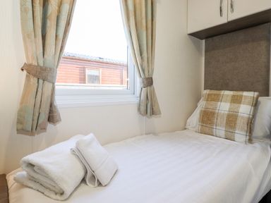 A single bed with a plaid pillow and folded white towels near a window with patterned curtains at Orion in Felmoor Park