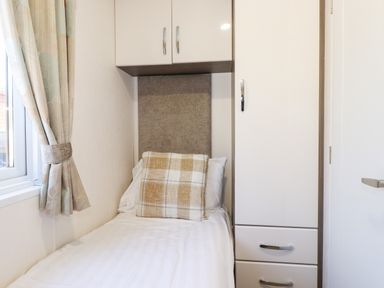 A single bed with a pillow and cushion next to a window and built in cupboard at Orion Felmoor Park
