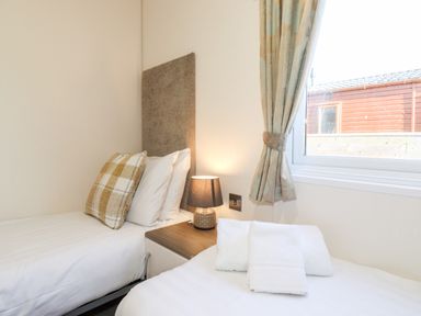 A bedroom with two single beds a bedside table lamp and a window with curtains at Orion in Felmoor Park